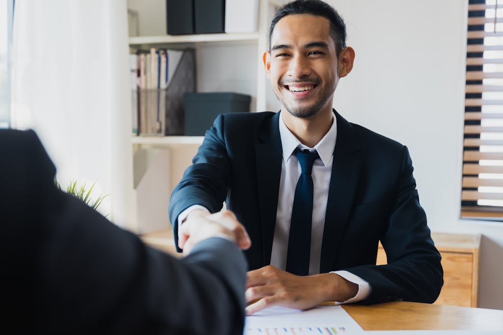 Confident businessman in suit shaking hands at office desk, symbolizing successful partnership.